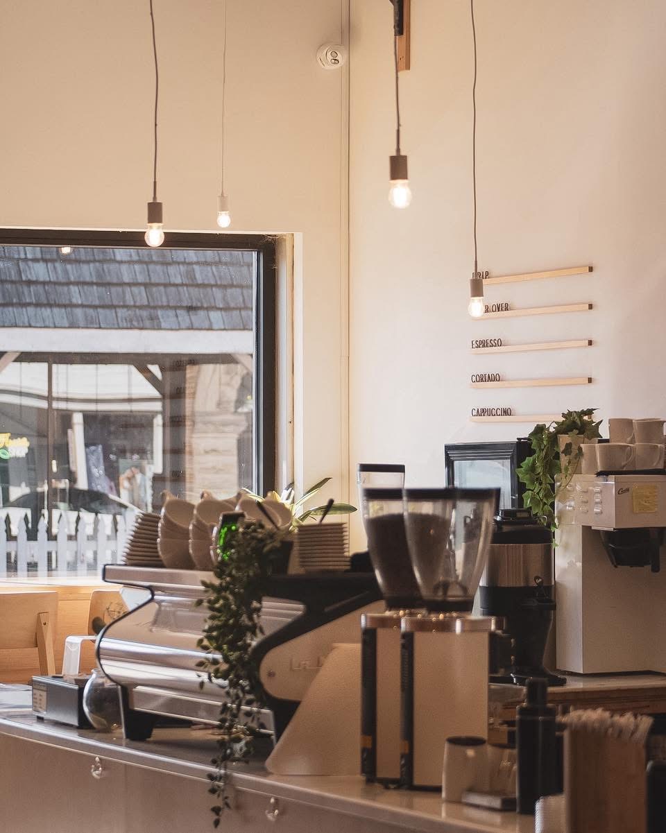 The café bar beside tall storefront windows, with the menu board and espresso setup.